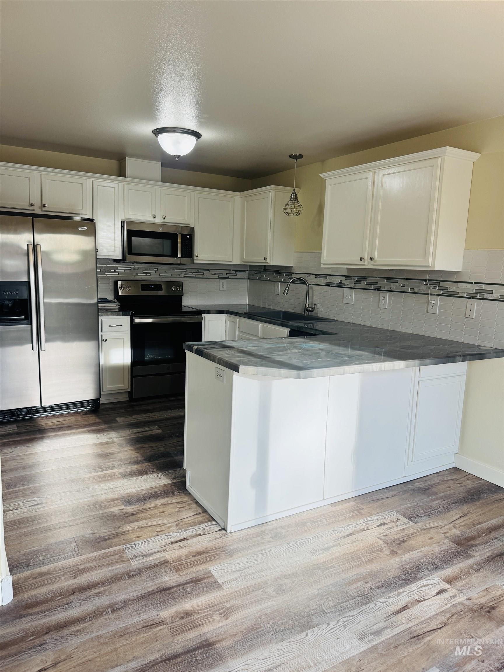 3203 South Capistrano Avenue Boise, ID 83705 - Photo 5 of 30 Kitchen with stainless steel appliances, a peninsula, white cabinetry, pendant lighting, and light wood-style flooring