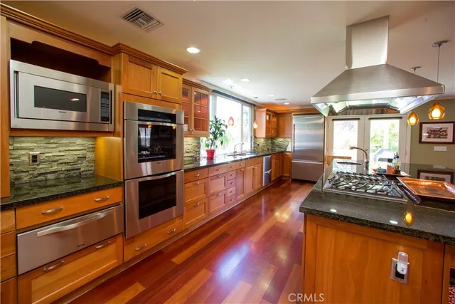 a kitchen with stainless steel appliances kitchen island granite countertop a stove and a wooden floors