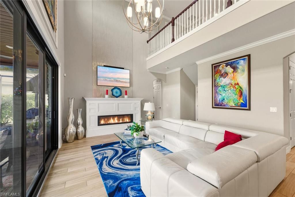 2115 Antigua Lane Naples, FL 34120 - Photo 13 of 41 Living area with a warm lit fireplace, a towering ceiling, light wood finished floors, ornamental molding, and arched walkways