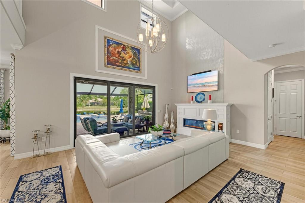 2115 Antigua Lane Naples, FL 34120 - Photo 14 of 41 Living room featuring crown molding, light wood-type flooring, a glass covered fireplace, a high ceiling, and arched walkways