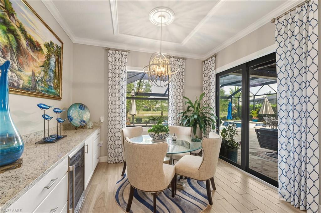 2115 Antigua Lane Naples, FL 34120 - Photo 15 of 41 Dining space featuring light wood-style flooring, plenty of natural light, wine cooler, ornamental molding, and a chandelier