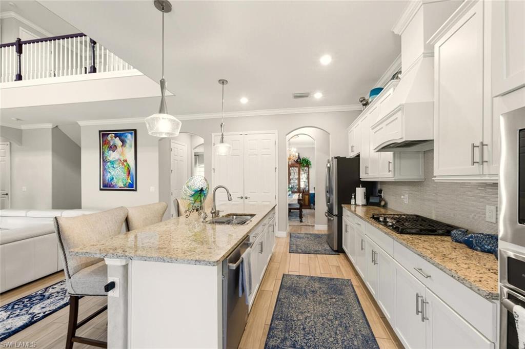 2115 Antigua Lane Naples, FL 34120 - Photo 16 of 41 Kitchen with a breakfast bar area, arched walkways, light stone counters, ornamental molding, and white cabinets