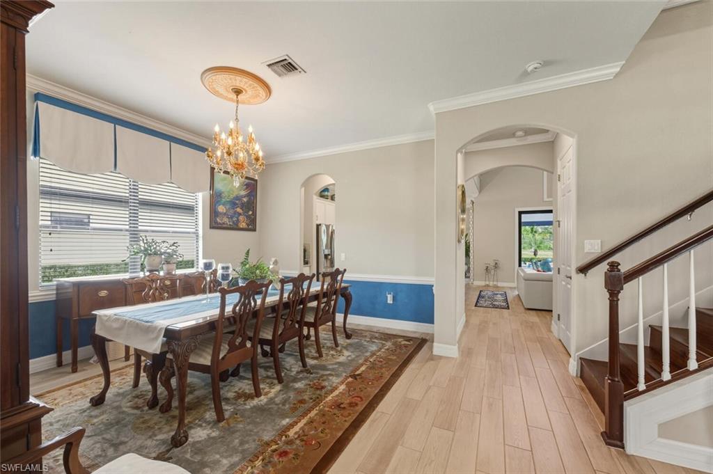 2115 Antigua Lane Naples, FL 34120 - Photo 10 of 41 Dining room featuring light wood finished floors, arched walkways, crown molding, stairs, and a chandelier
