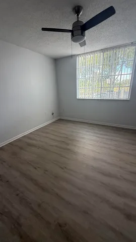 an empty room with wooden floor chandelier fan and windows