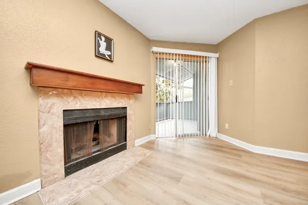 a view of an empty room with wooden floor and a fireplace