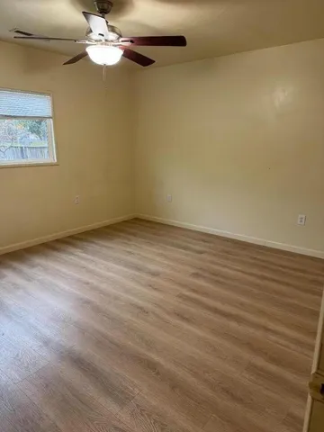 an empty room with wooden floor chandelier fan and windows