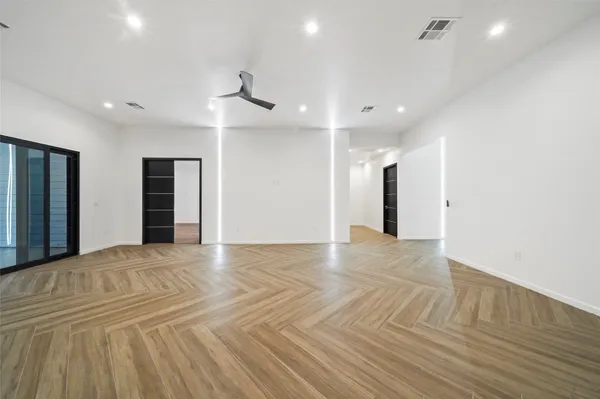 a view of an empty room with wooden floor and a ceiling fan
