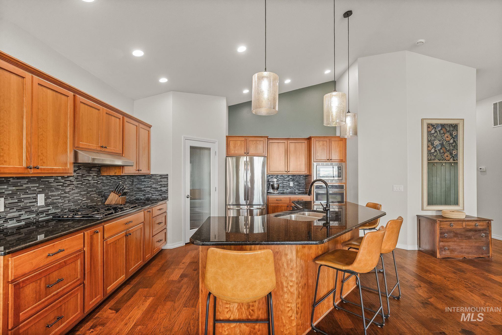 602 Quarry Road Asotin, WA 99402 - Photo 11 of 49 Spacious kitchen featuring rich wood cabinetry, dark stone countertops, a tile backsplash, stainless steel appliances, and a central island with pendant lighting