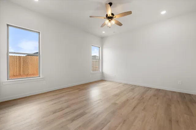 an empty room with wooden floor chandelier fan and windows