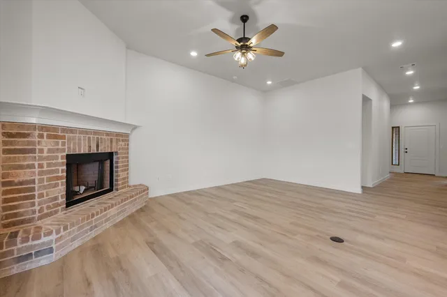 a view of an empty room with wooden floor fireplace and a window