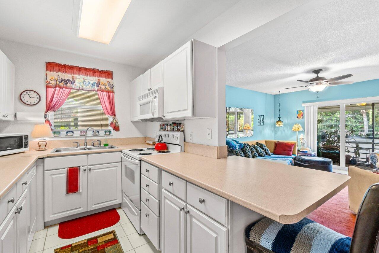 1124 Northwest 13th Street, Unit 204A Boca Raton, FL 33486 - Photo 3 of 30 a kitchen with kitchen island a stove a sink dishwasher and white cabinets with wooden floor