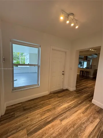 a view of an empty room with wooden floor and a window