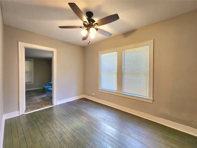 an empty room with wooden floor fan and windows