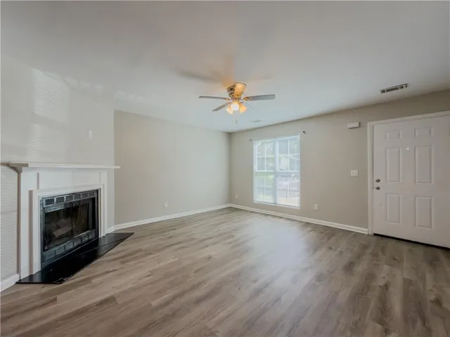a view of an empty room with wooden floor fireplace and a window
