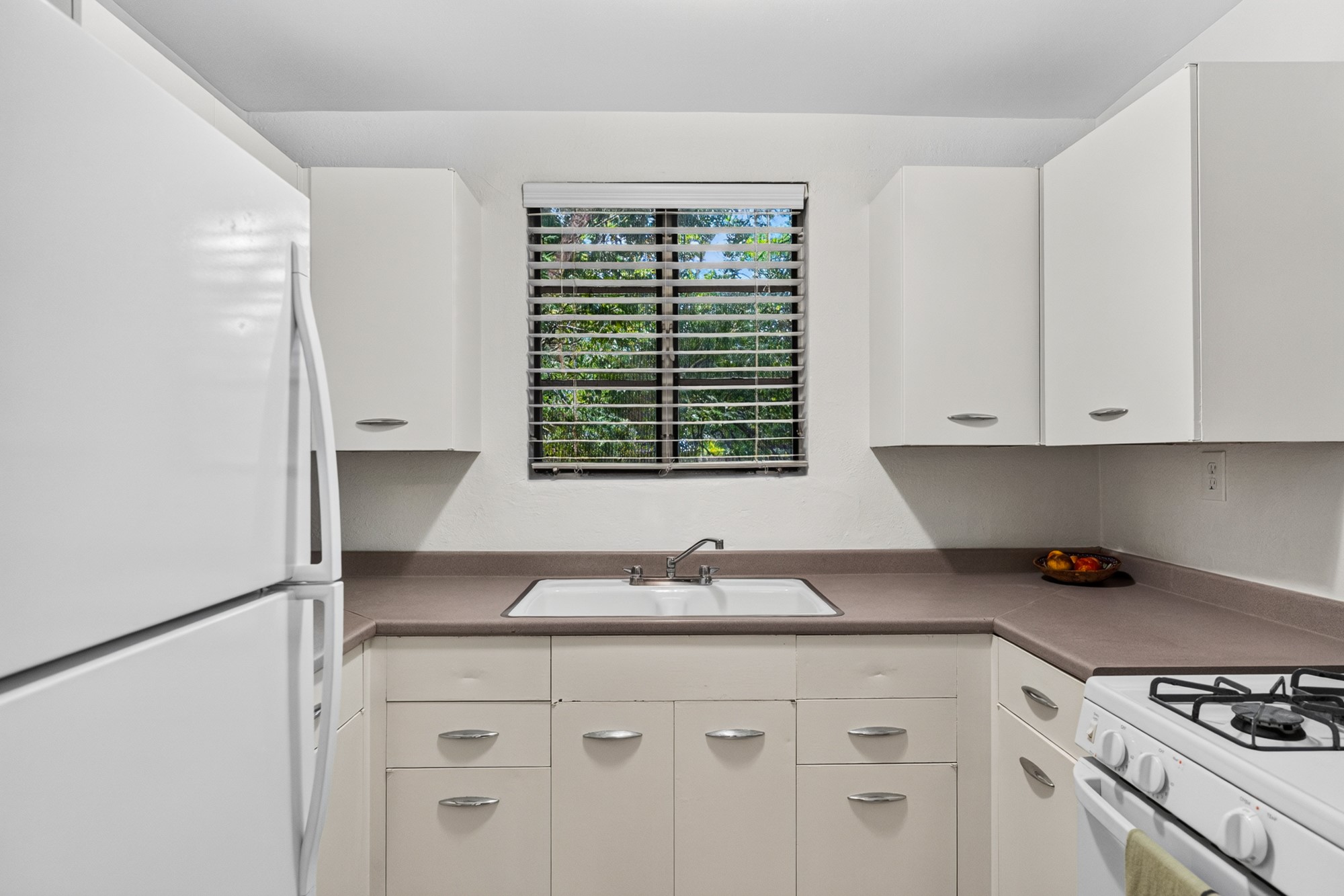 1302 Kirkwood Road, Unit B Austin, TX 78722 - Photo 8 of 21 Functional kitchen with ample cabinet space, a pristine white sink, and a view of verdant foliage.