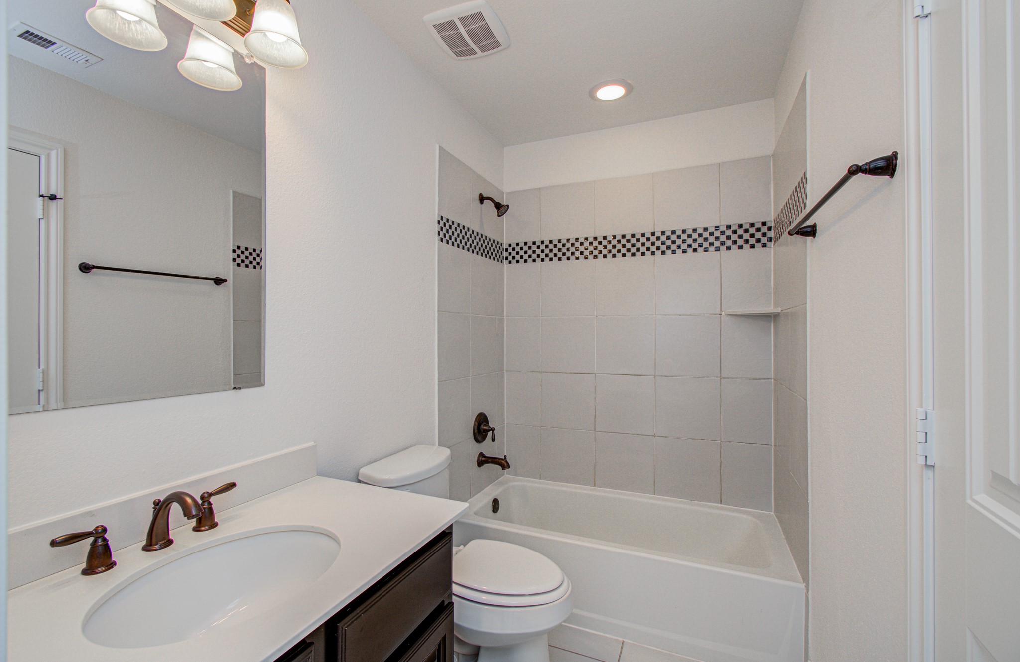 6621 North Main Street Houston, TX 77009 - Photo 25 of 41 Personal bathroom bathroom conveniently connected to the third floor secondary bedroom features a clean, modern design with a tiled shower and bathtub combination. It includes a vanity with a dark wood finish, a white countertop, and bronze fixtures. The room is well-lit with overhead lighting and has a neutral color palette.