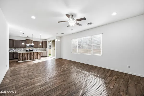 a view of an empty room with wooden floor and a kitchen