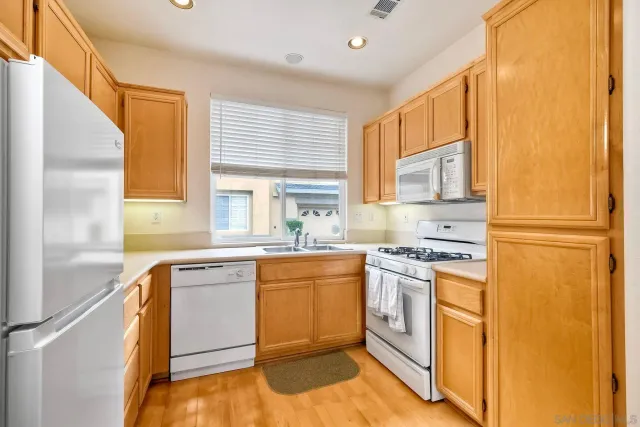 a kitchen with stainless steel appliances granite countertop a refrigerator a sink dishwasher a stove with white cabinets and wooden floor