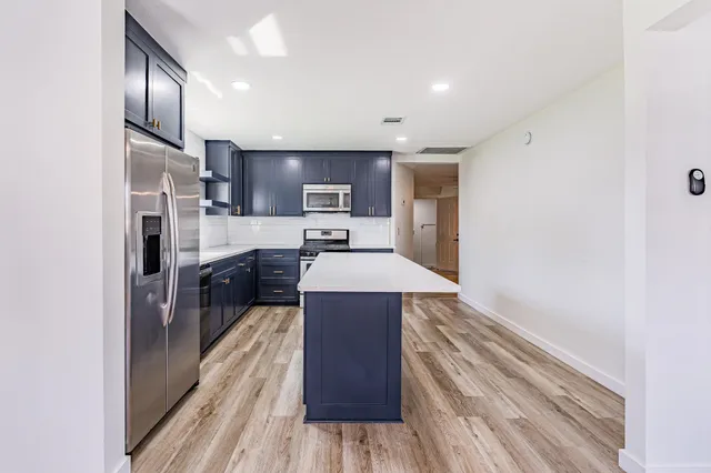 a kitchen with kitchen island wooden floors appliances and cabinets