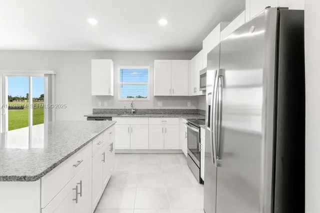 a kitchen with granite countertop a refrigerator and white cabinets