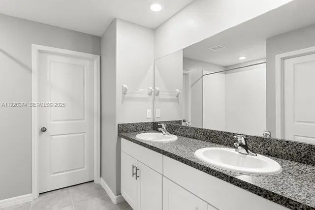 a bathroom with a granite countertop double vanity sink and a mirror