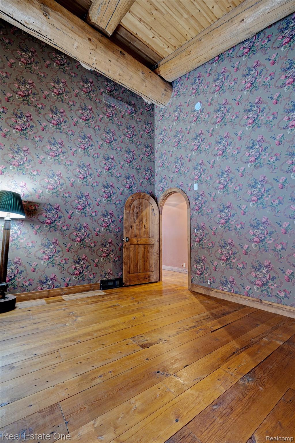 4340 Lahring Road Holly, MI 48442 - Photo 34 of 89 Empty room featuring light wood-style floors, wallpapered walls, a wooden ceiling with exposed beams, and arched walkways