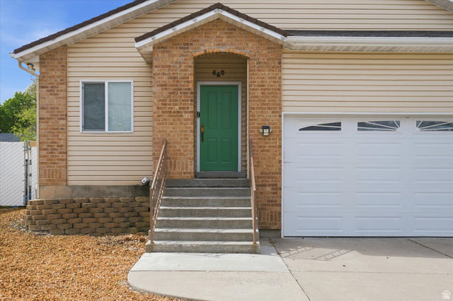 560 East 700 North Logan, UT 84321 - Photo 2 of 32 Exterior featuring a green entry door with side brick accents, concrete steps with metal railings, a white garage door with upper window inserts, and light-toned siding