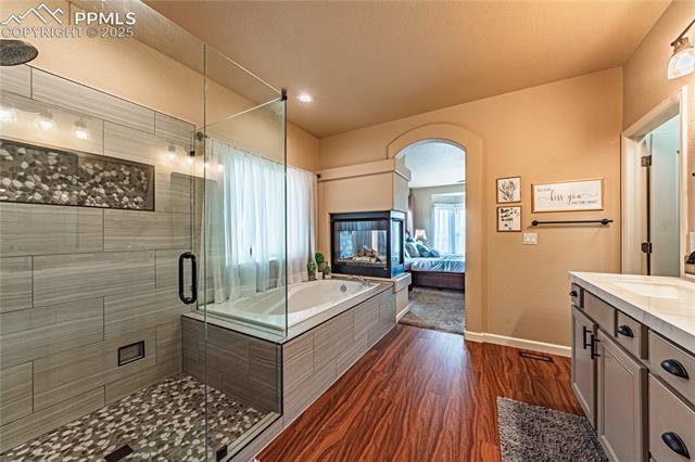 13812 Windy Oaks Road Colorado Springs, CO 80921 - Photo 26 of 50 Full bathroom featuring vanity, baseboards, a stall shower, a garden tub, and wood finished floors
