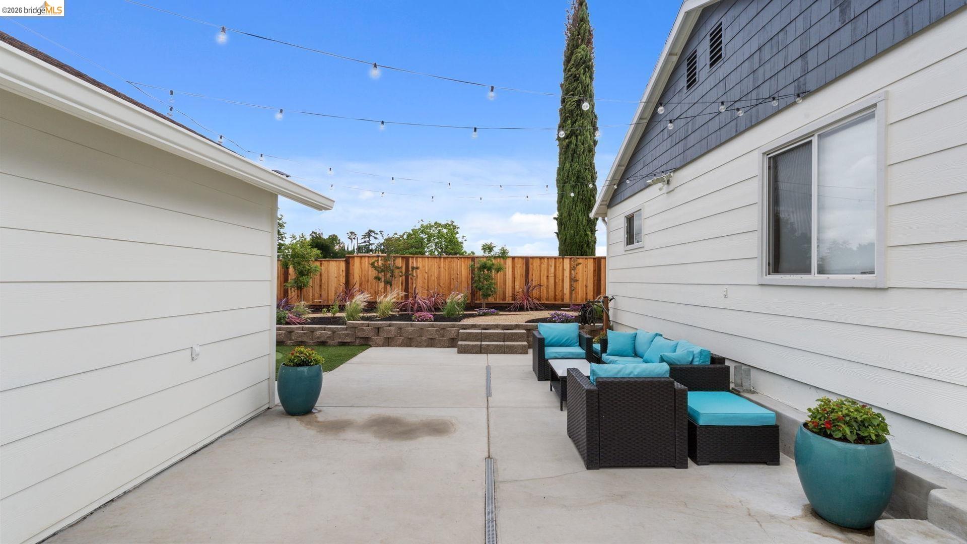 700 Brownstone Road Oakley, CA 94561 - Photo 35 of 58 Hardscaped patio with string lighting, multiple tiered garden beds, wooden privacy fencing, and exterior house siding