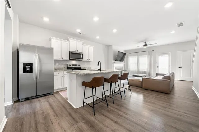 a kitchen with stainless steel appliances kitchen island granite countertop a refrigerator a stove a sink a dining table and chairs with wooden floor