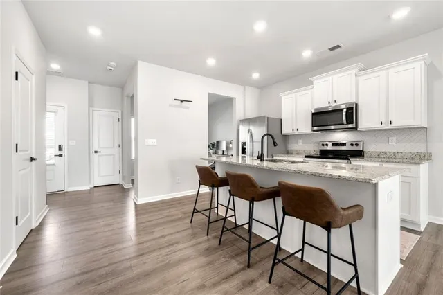 a kitchen with stainless steel appliances granite countertop a stove top oven a sink a refrigerator with white cabinets and wooden floor