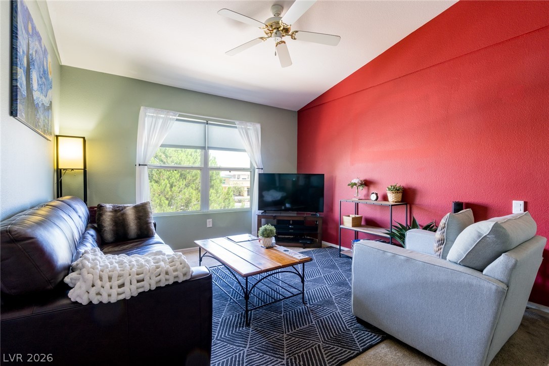 Living area featuring vaulted ceiling, dark carpet, and ceiling fan