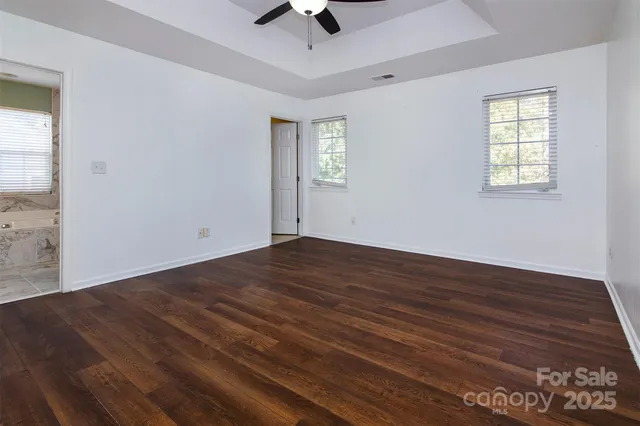 an empty room with wooden floor chandelier fan and windows
