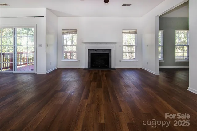 an empty room with wooden floor fireplace and windows