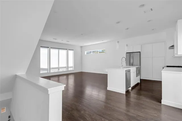 a view of empty room with wooden floor and kitchen
