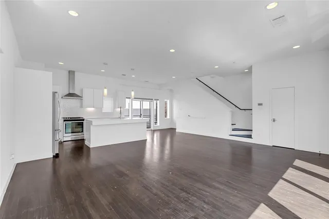 a view of an empty room and kitchen with wooden floor