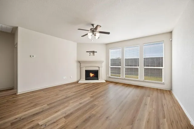 a view of an empty room with wooden floor fireplace and a window