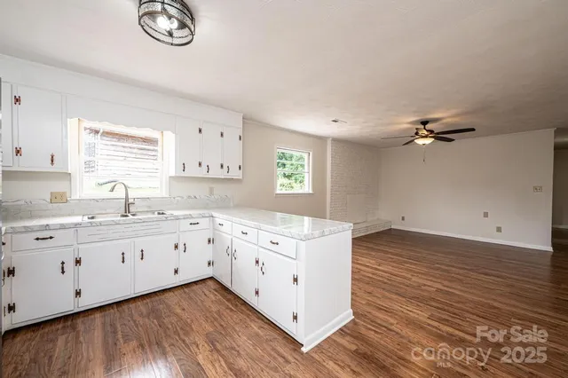 a kitchen with granite countertop a stove a sink and white cabinets with wooden floor