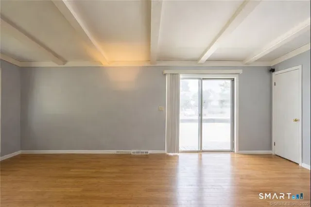 a view of an empty room with window and wooden floor