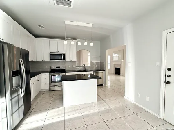 a large kitchen with kitchen island granite countertop a refrigerator a sink a stove a dining table and chairs