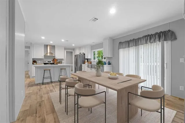 a kitchen with stainless steel appliances kitchen island granite countertop a dining table chairs and a refrigerator
