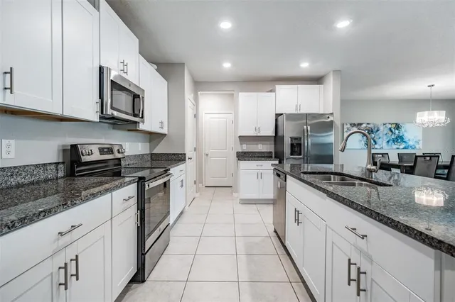 a kitchen with stainless steel appliances granite countertop a stove a sink a microwave a refrigerator and white cabinets