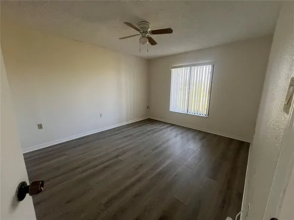 an empty room with wooden floor fan and windows
