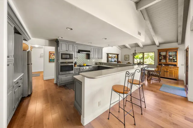 a kitchen with stainless steel appliances kitchen island granite countertop a refrigerator a stove a dining table and chairs with wooden floor