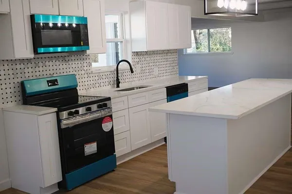 a kitchen with a sink dishwasher a stove and white cabinets with wooden floor