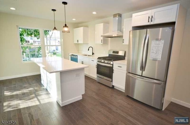 a kitchen with stainless steel appliances granite countertop a refrigerator a stove a sink and a wooden floor