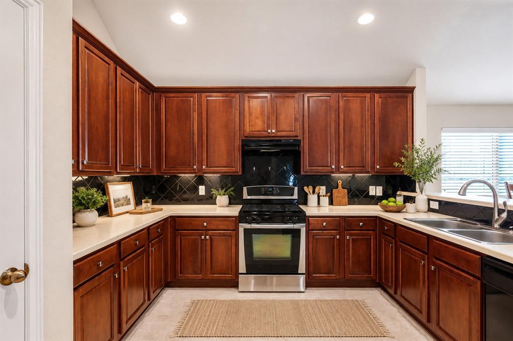 5316 Ridgeson Drive McKinney, TX 75071 - Photo 3 of 33 U-shaped kitchen featuring dark wood cabinetry, light countertops, black tile backsplash, stainless steel range, and a double basin sink