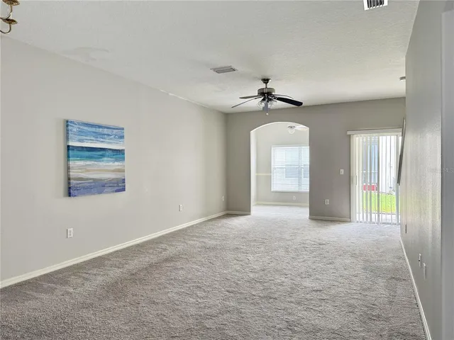 an empty room with chandelier fan and windows
