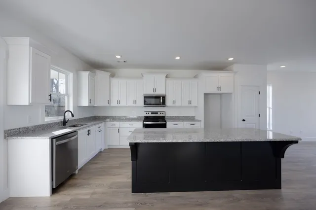 a large kitchen with stainless steel appliances kitchen island granite countertop a stove a sink a refrigerator and white cabinets