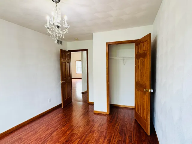 an empty room with wooden floor chandelier and windows